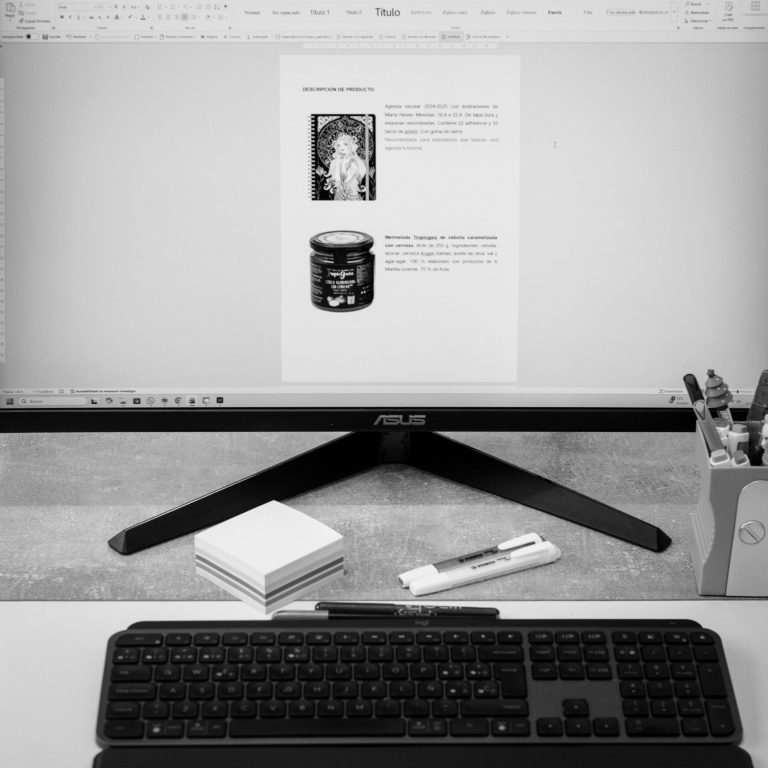 Pantalla de ordenador mostrando un documento con texto e imágenes, teclado y objetos de oficina.